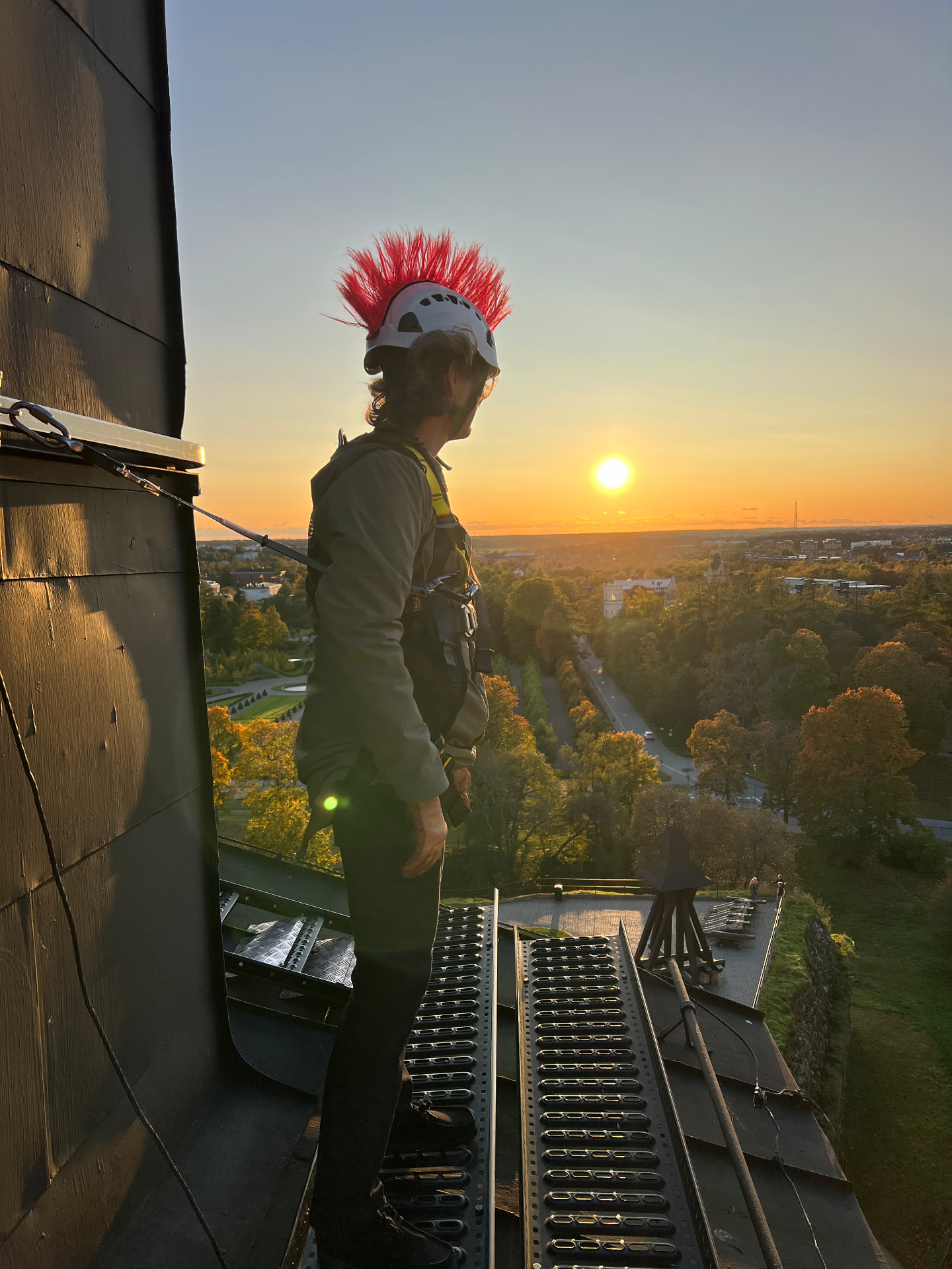 Takvandrare i hjälm och sele på gångbryggan på Uppsala slotts tak i solnedgången